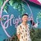 A person stands in front of a turquoise wall adorned with colorful tropical decor, featuring the word "High" in cursive, reminiscent of a vibrant auto body shop waiting area.
