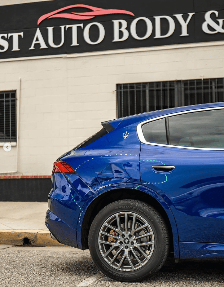 A blue car with visible dents and damages on its rear side is parked in front of a Century1st Auto Body Shop & Paint sign.