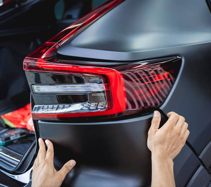 Hands applying a protective film to the taillight of a black car at a certified Toyota Collision Repair body shop.