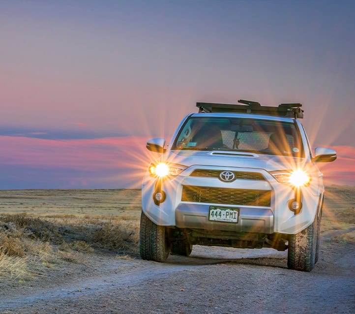 A silver Toyota SUV with headlights on is driving on a dirt road at sunset, looking pristine thanks to recent Toyota Collision Repair at a certified body shop.